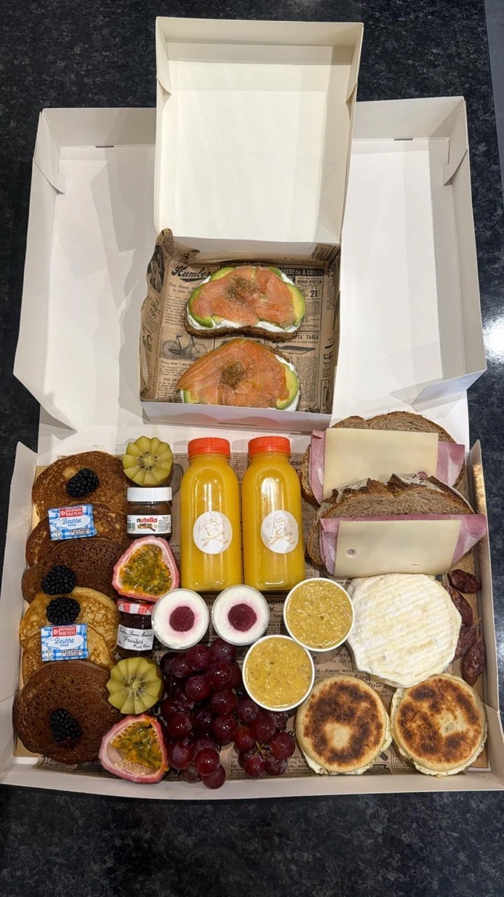 Brunch box gourmet avec pancakes, boissons, saumon, pains, fromage et fruits