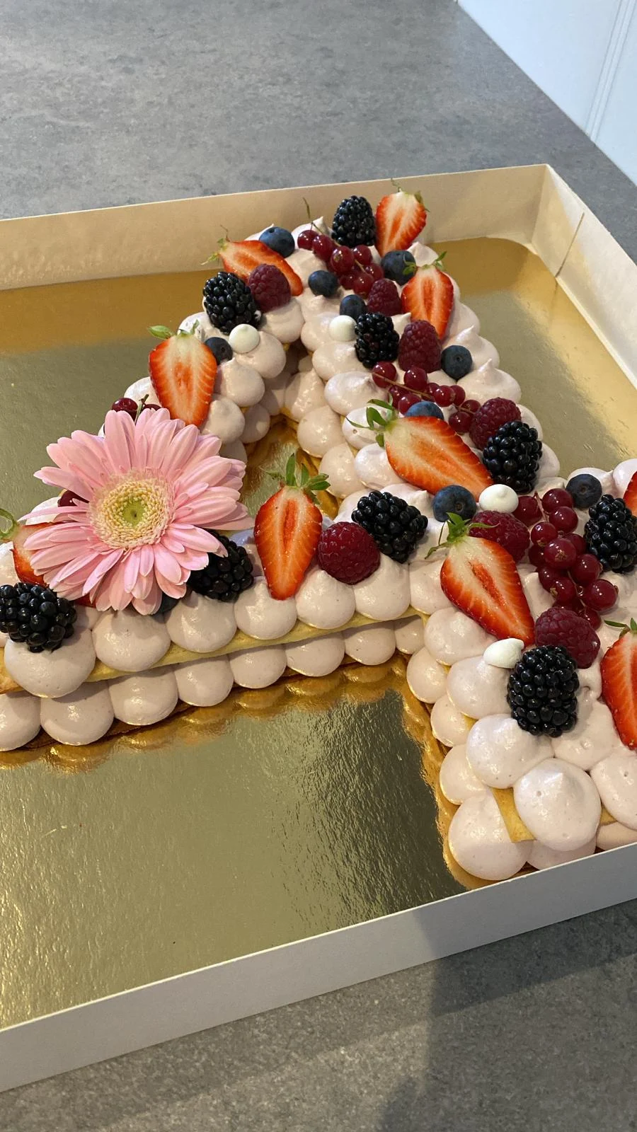 Number cake en forme de A garni de fruits rouges et d’une fleur rose